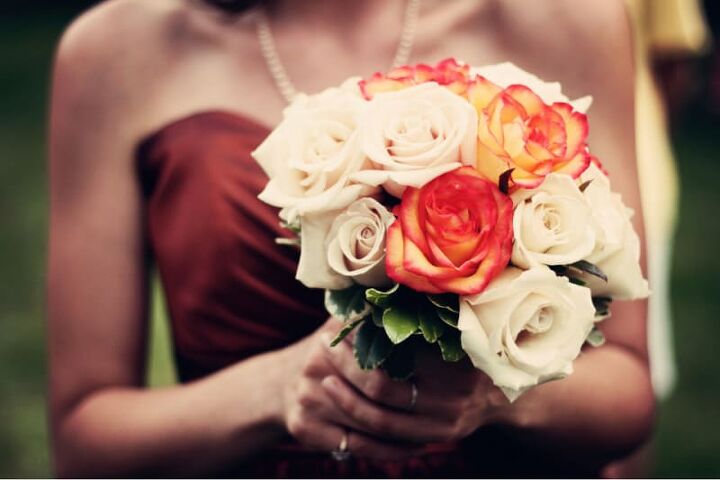 fall wedding ideas on a budget, a woman in a maroon dress holding cream and orange roses