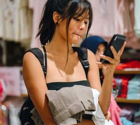 10 tips for being fashionable on a budget, a woman holding a stack of clothes looking at her phone