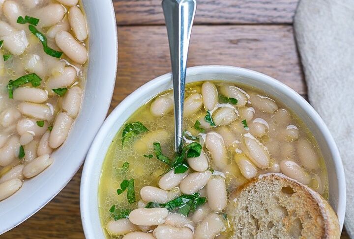 groceries to buy on a budget eat well for less, Brothy Beans in a white bowl beans are a great grocery to buy on a budget
