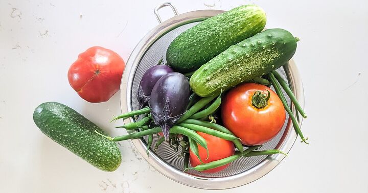 groceries to buy on a budget eat well for less, Vegetables from the garden in a colander on a white counter growing vegetables help keep your grocery budget low