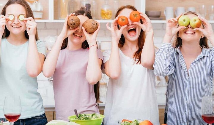 budget grocery list the best cheapest foods for tight budgets, 4 young women in kitchen laughing with vegetables against their eyes