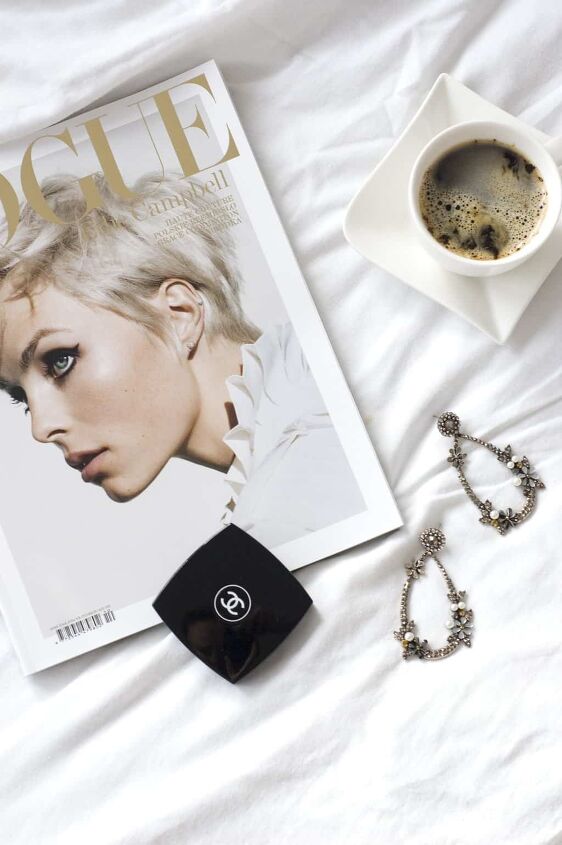 things to stop buying to save money, magazine on a white bed with jewelry and coffee