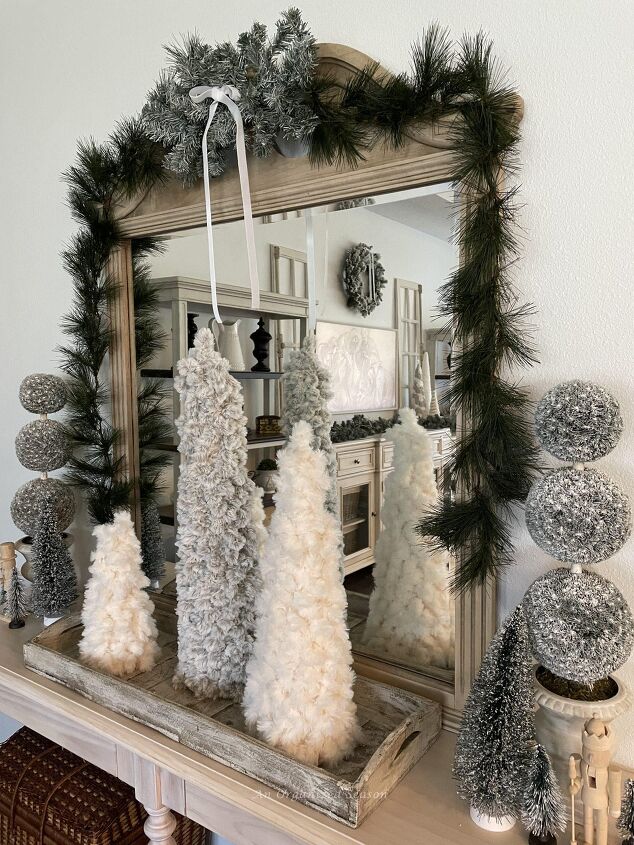 seven ways to decorate for christmas on a budget, A console table and mirror decorated with evergreen garland yarn cone trees topiaries bottle brush trees and nutcrackers