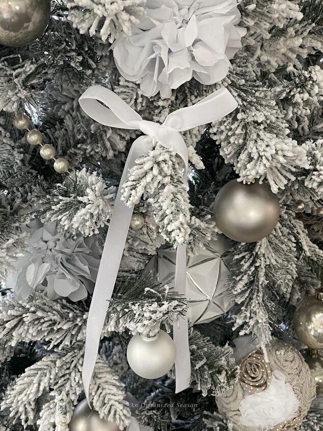 seven ways to decorate for christmas on a budget, A white velvet bow hanging on a Christmas tree branch