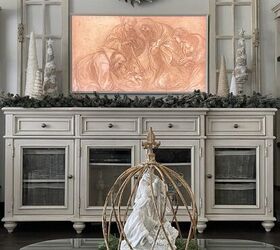 seven ways to decorate for christmas on a budget, A cream console table with a picture frame tv hanging above it displaying the Holy Family