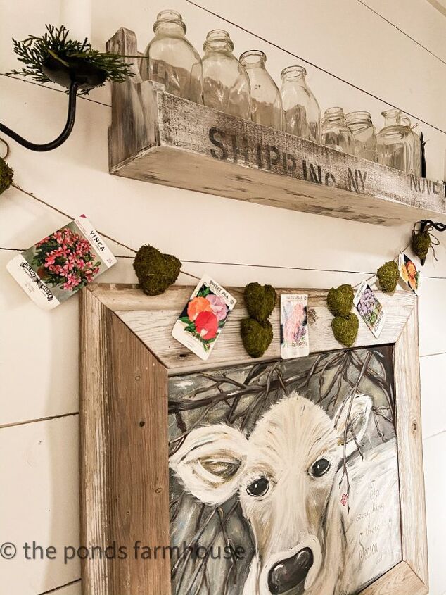 the best thrifted valentine s decor ideas, Vintage Seed Packet and moss heart garland over Faith Cow Painting