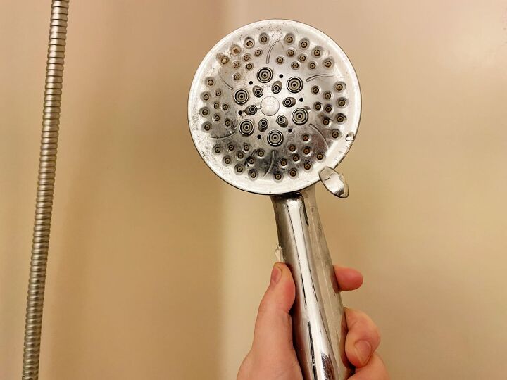 bathroom repairs to try yourself before you call a plumber, Hand holding a clogged shower head in a walk in shower tub combo