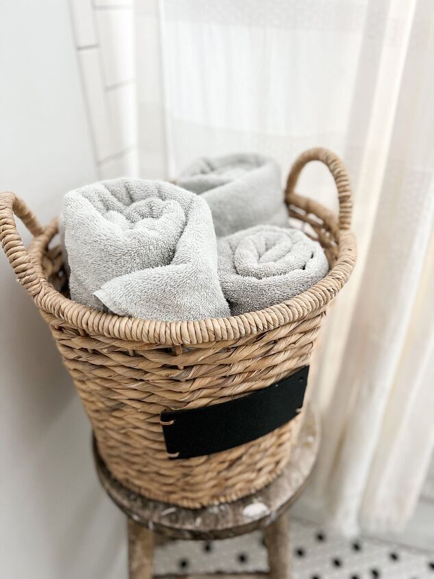 simple decor series how to decorate a small bathroom on a budget, Sturdy wicker basket holds rolled up white towels on vintage wooden stool complete with decades old paint spots