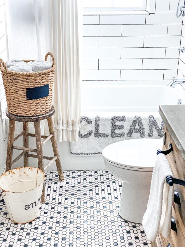 simple decor series how to decorate a small bathroom on a budget, Showing the white shower curtain with white bathmat gray CLEAN letters hung neatly over bathtub A wicker basket of towels sits on a vintage wooden stool besides the tub