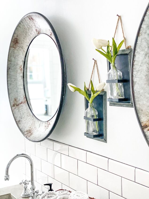simple decor series how to decorate a small bathroom on a budget, Neatly installed white subway tile form a backsplash behind the two matching sinks Two pieces of wall art with faux tulips hang on the wall above between two matching galvanized oval mirrors
