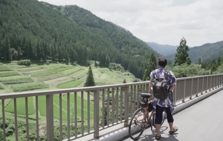 japanese minimalist lifestyle does minimalism save money, Man standing with a bike on a bridge overlooking mountains